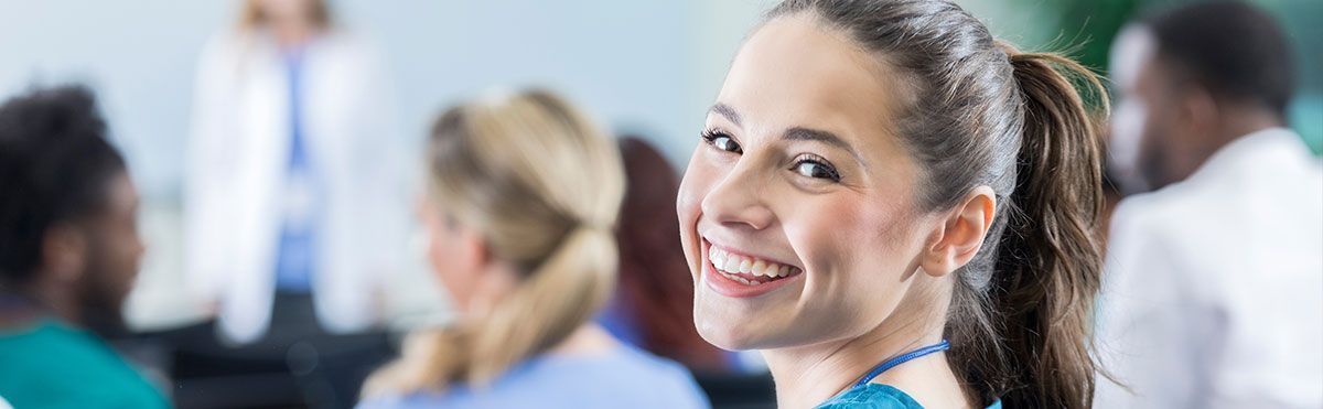 Una mujer sonríe frente a un grupo de personas en un salón de clases.