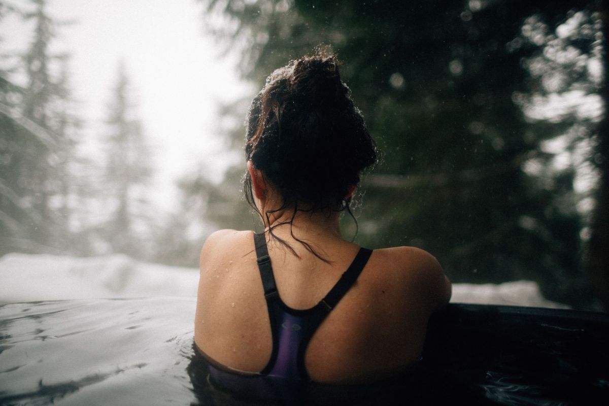 A woman is sitting in a hot tub with trees in the background.