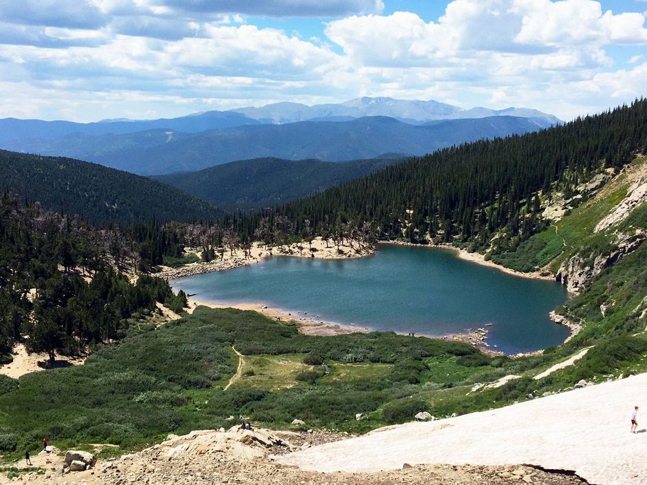 A lake in the middle of a forest with mountains in the background.