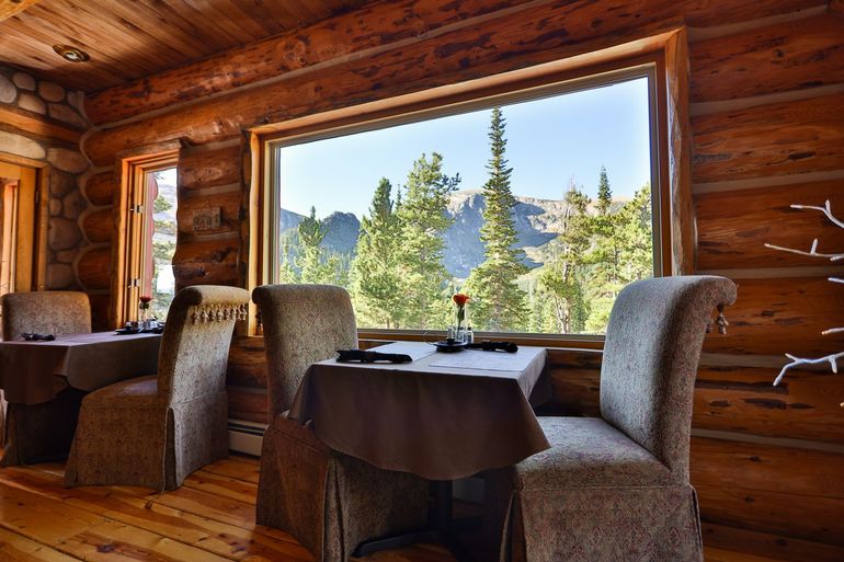 Two tables and chairs in a log cabin with a view of the mountains.