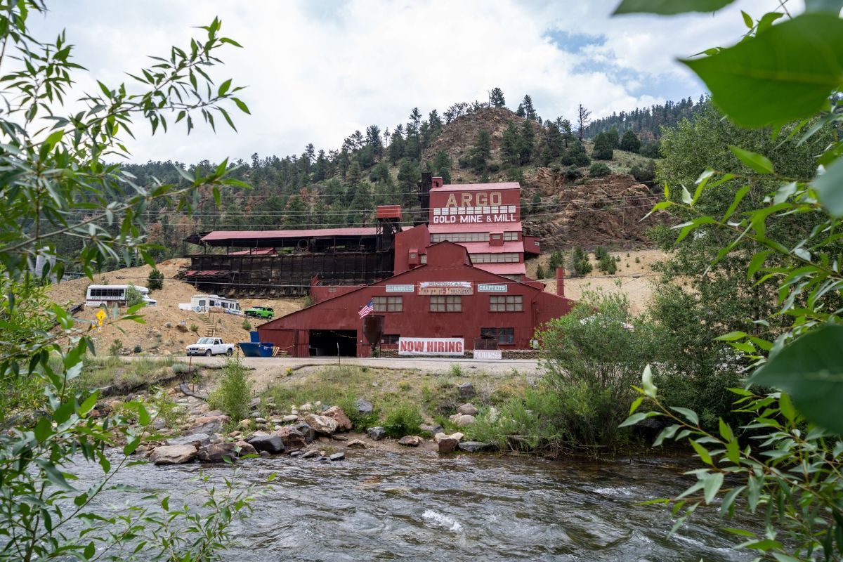 A large red building is sitting next to a river in the middle of a forest.