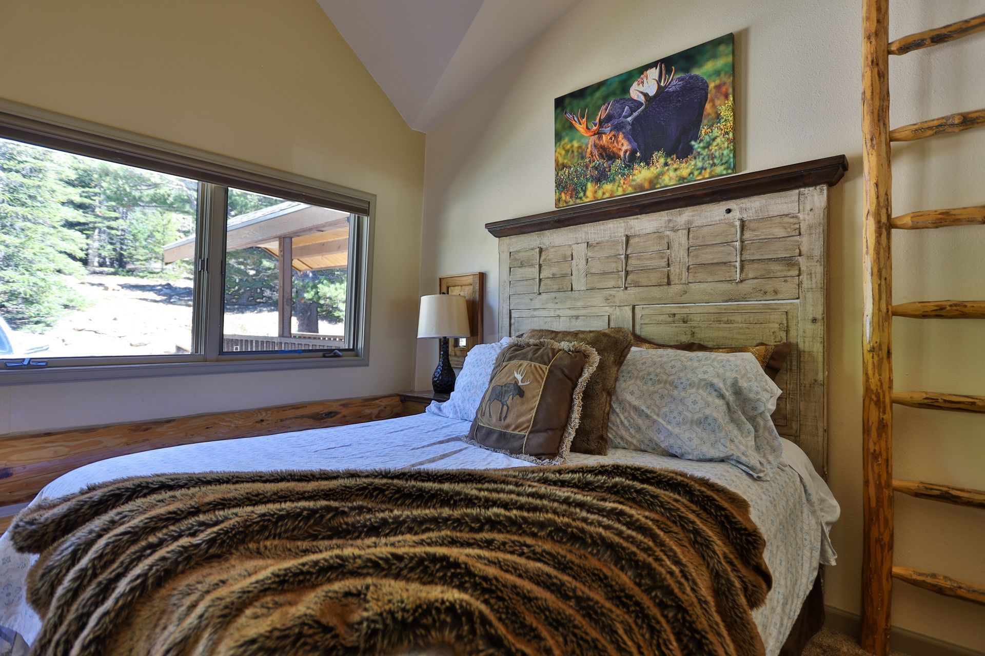 A bedroom with a bed , ladder and a painting on the wall.