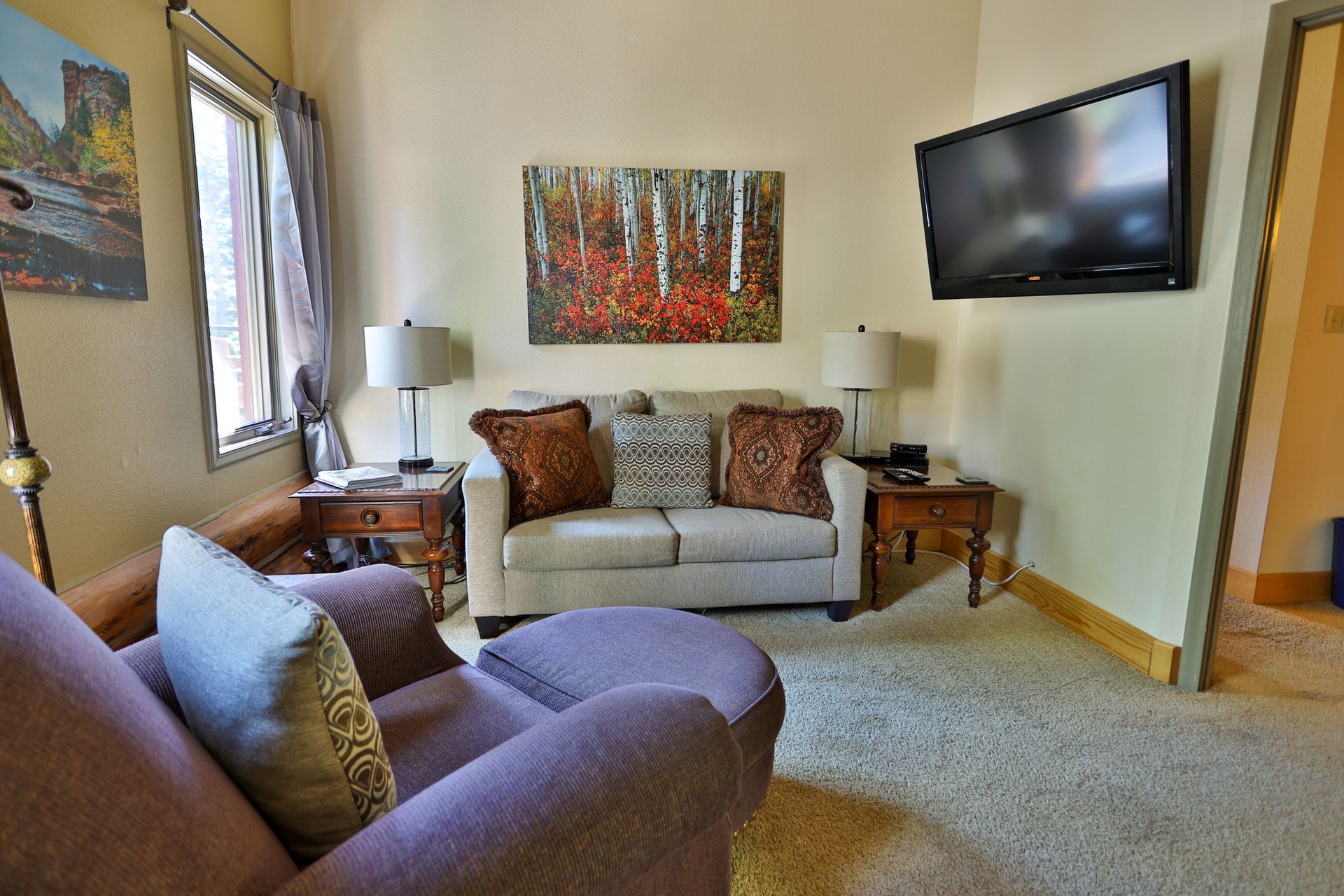 A living room with a couch , chair , ottoman and television.