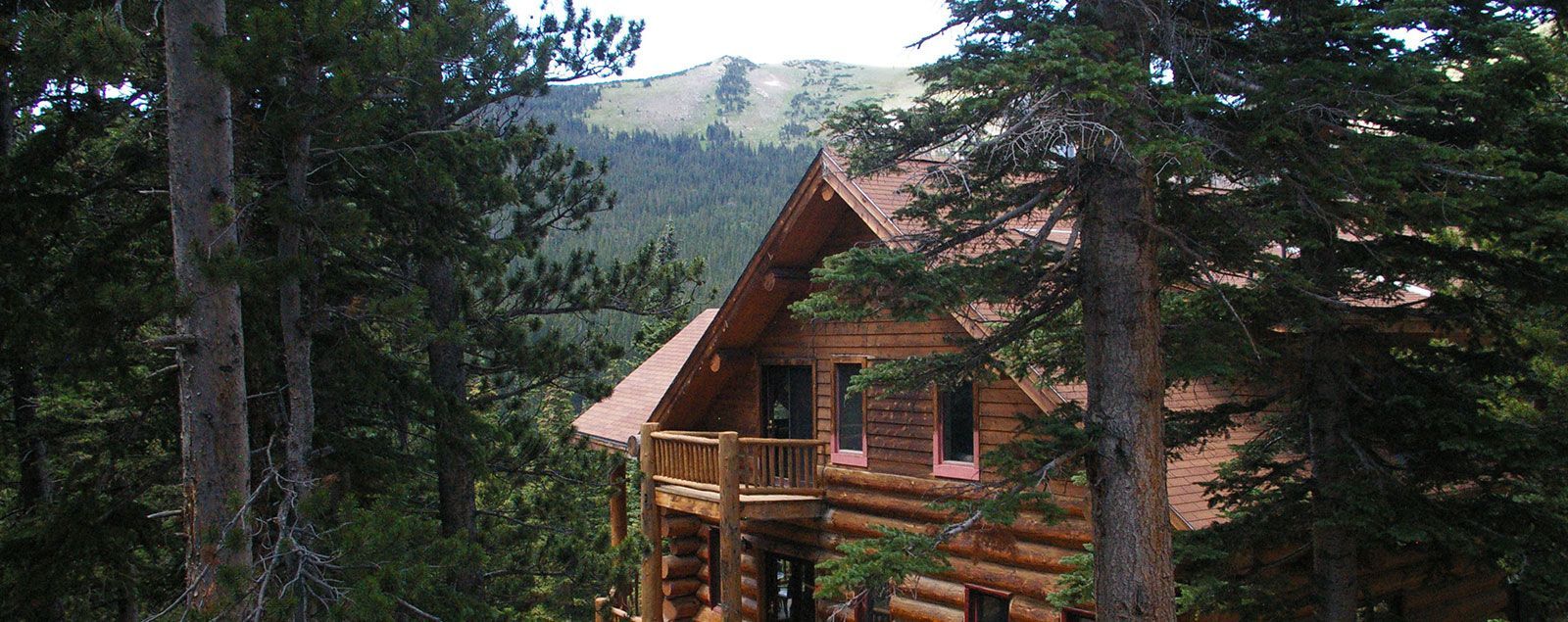A log cabin in the middle of a forest with mountains in the background