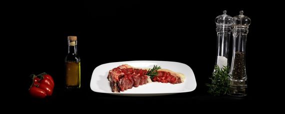 Natura morta con tartare di manzo, condimenti e olio su sfondo nero.