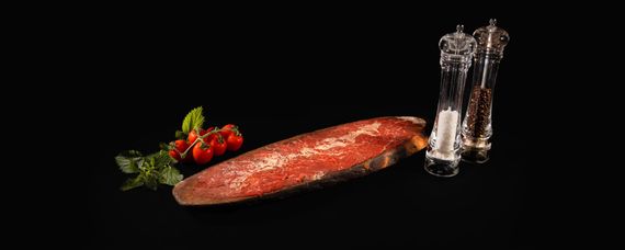 Carne cruda e una mannaia su una tavola di legno su uno sfondo nero.