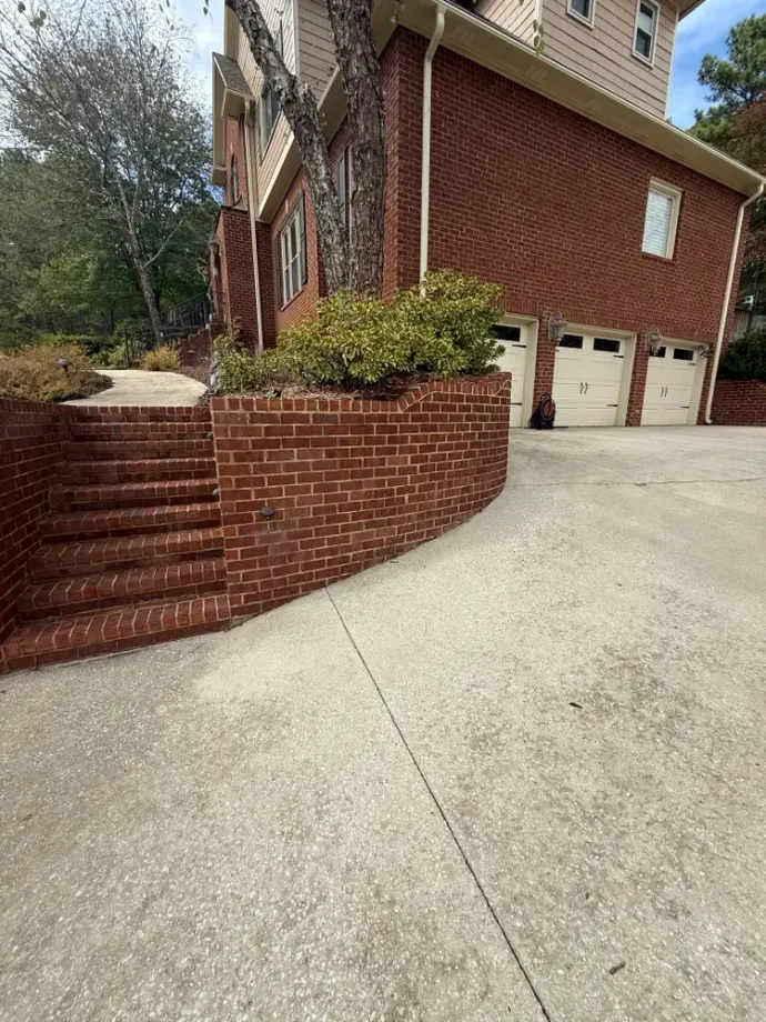 Brick house with stairs leading up from a concrete driveway. Garage visible.