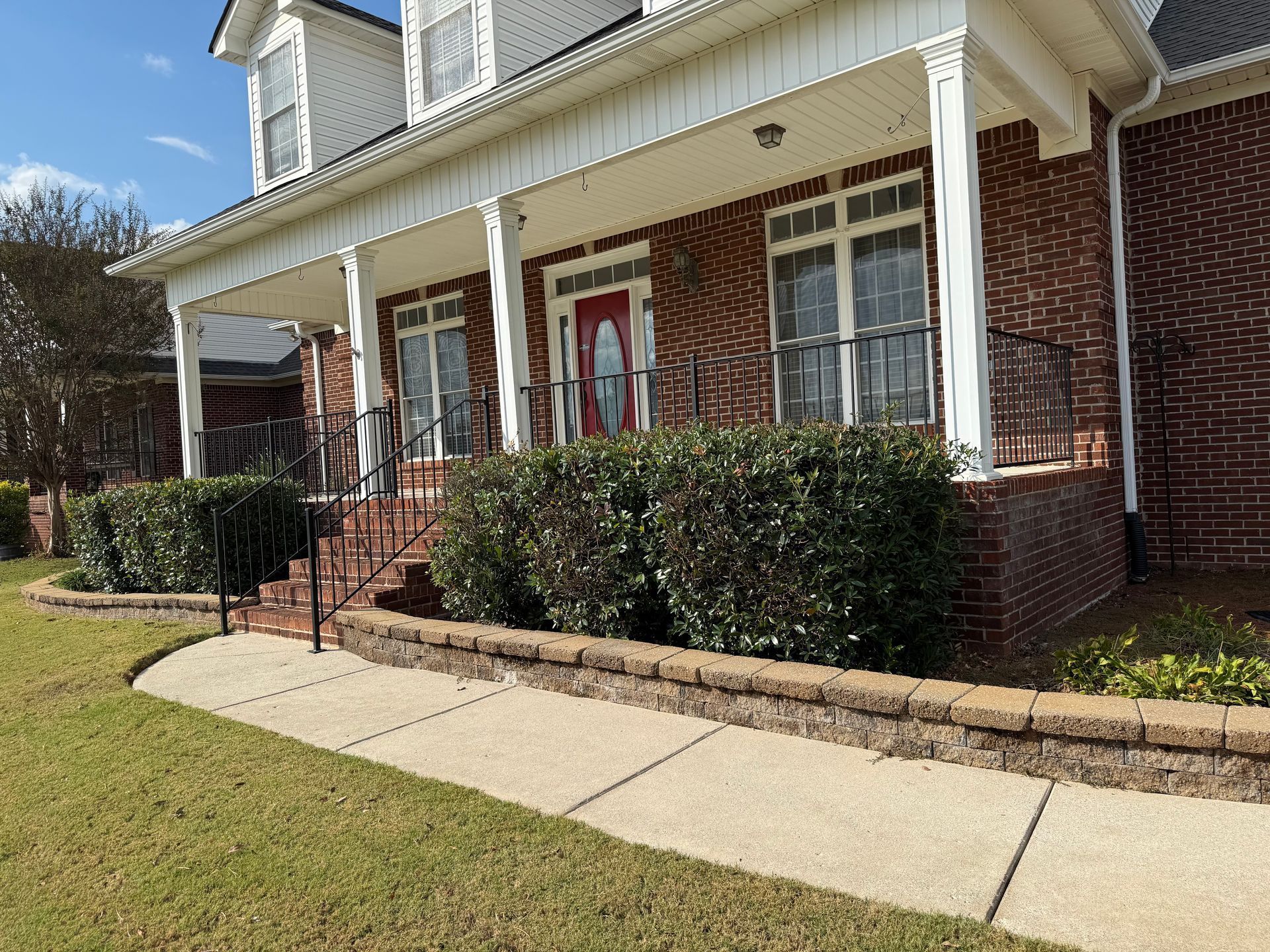 Brick house with porch, landscaping, and sidewalk.