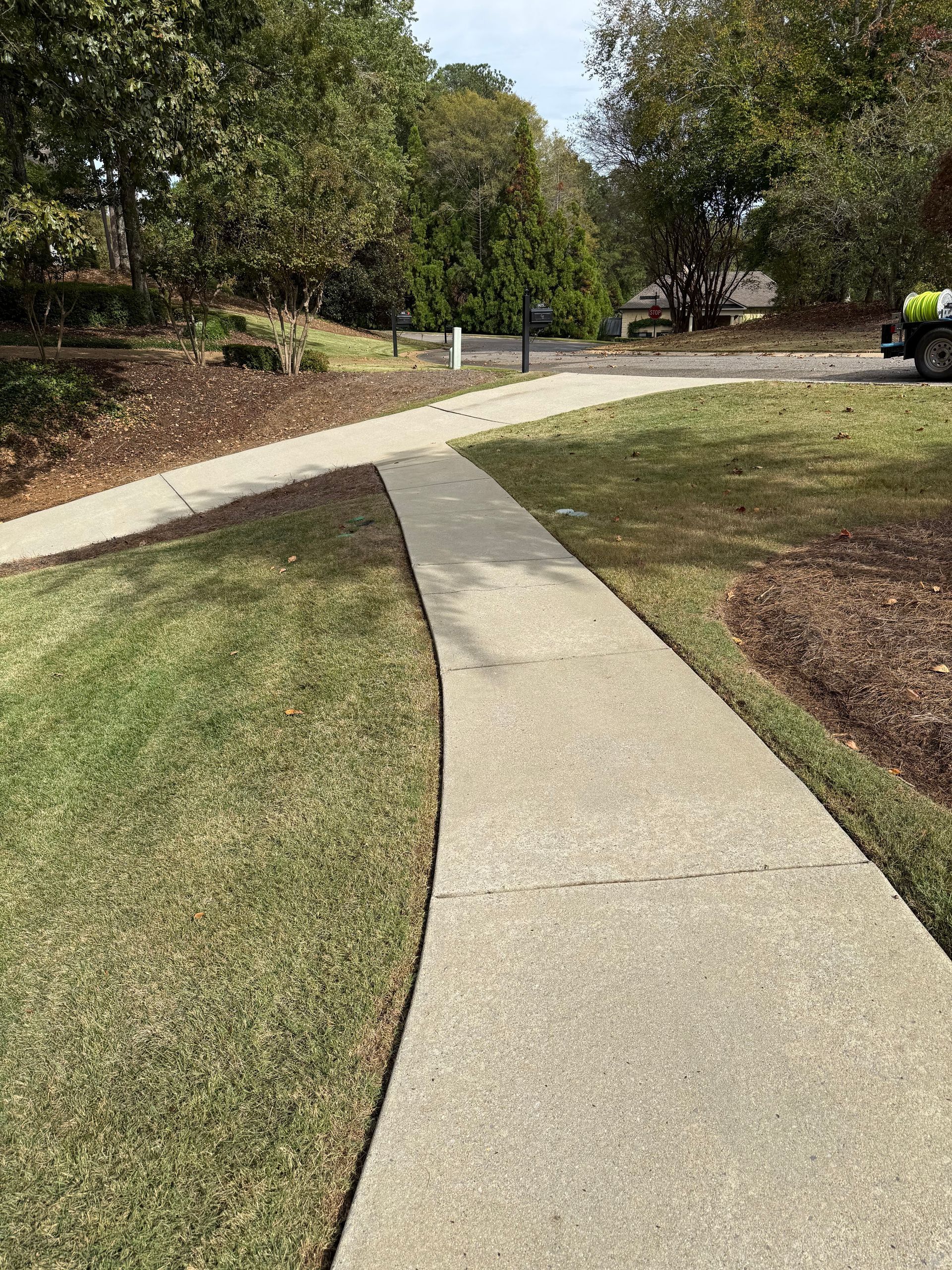 Concrete sidewalk curving through a grassy area, leading toward trees and a building.