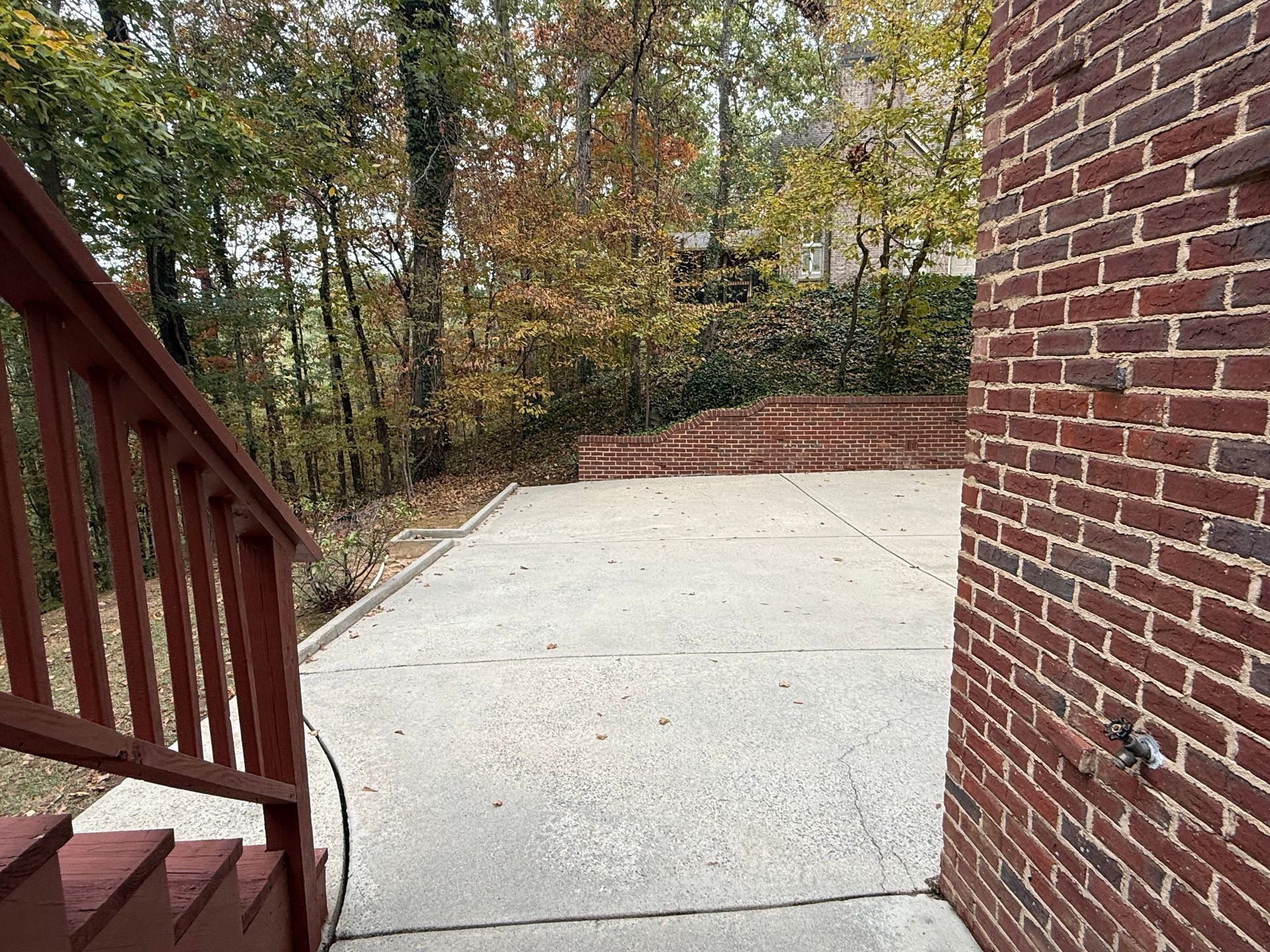 Concrete patio with stairs, brick wall, and wooded area in background.