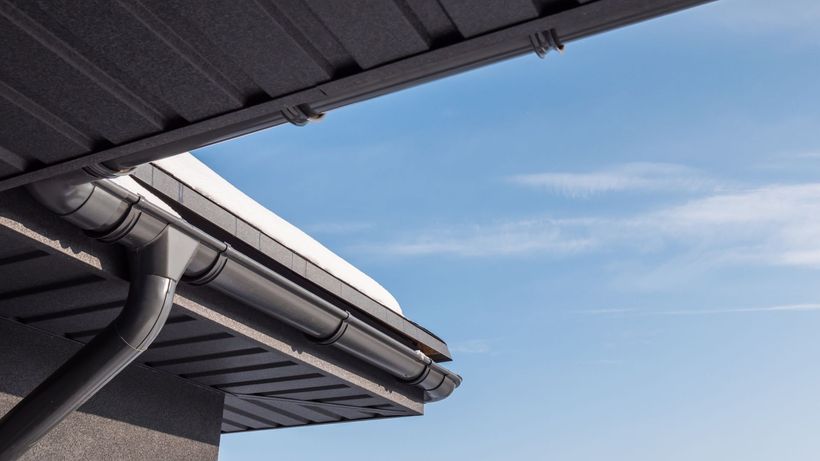 A close up of a gutter on a roof with a blue sky in the background.