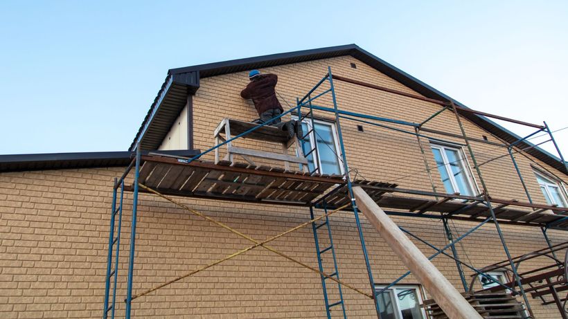 A man is standing on a scaffolding on the side of a brick building.