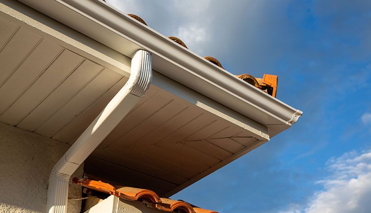 A white gutter on the side of a house with a tiled roof.