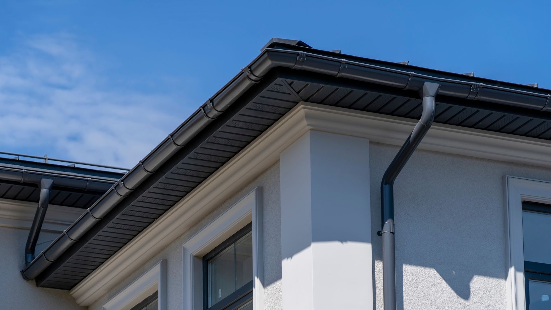 A white house with a black gutter on the roof.