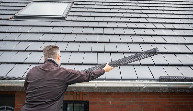 A man is cleaning the roof of a house with a broom.