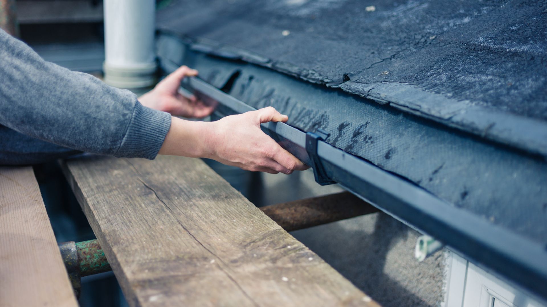 A person is fixing a gutter on a roof.