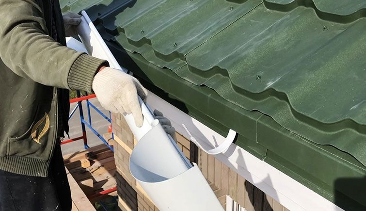 A man is fixing a gutter on a green roof.