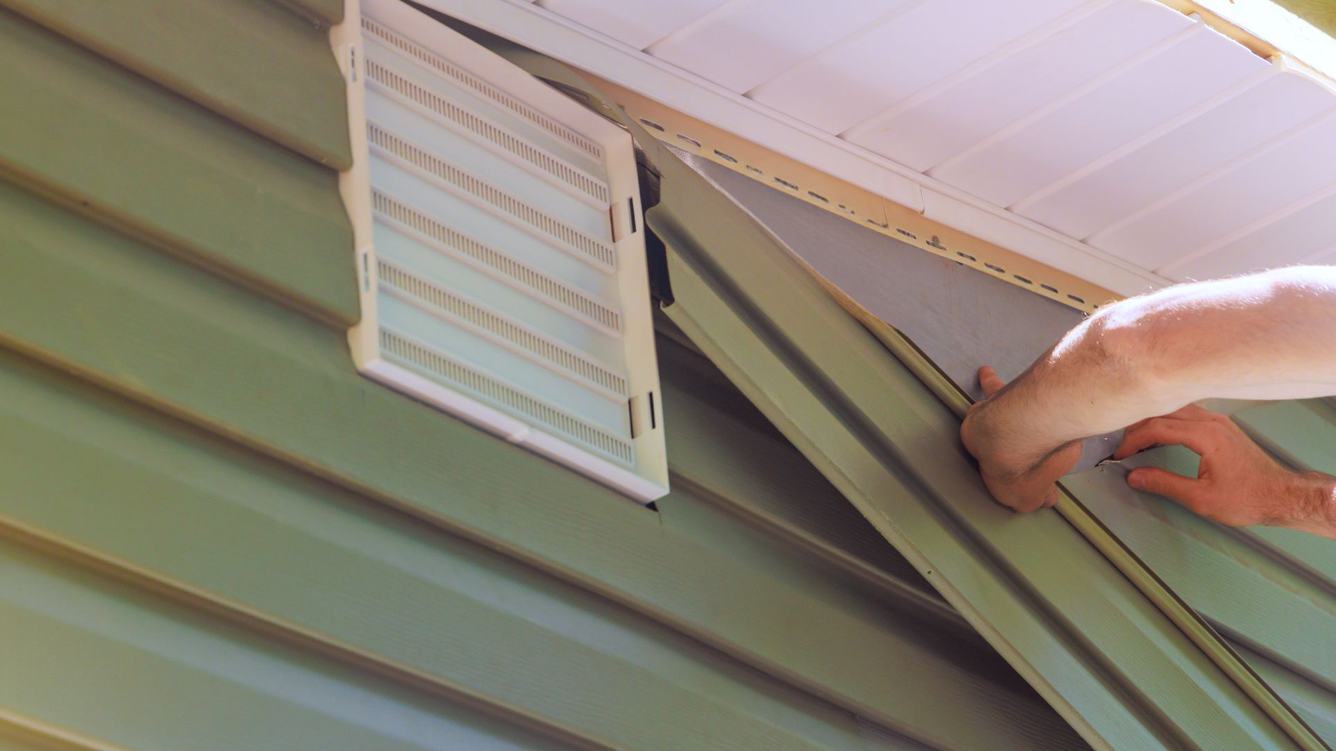 A person is installing a vent on the side of a house.