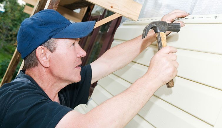 A man is using a hammer to fix a siding on a house.