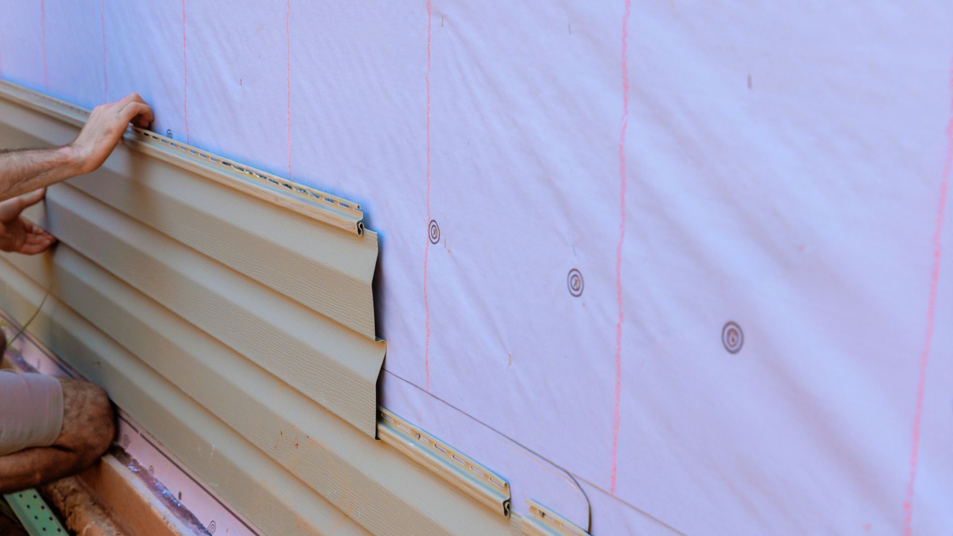 A man is installing siding on the side of a house.