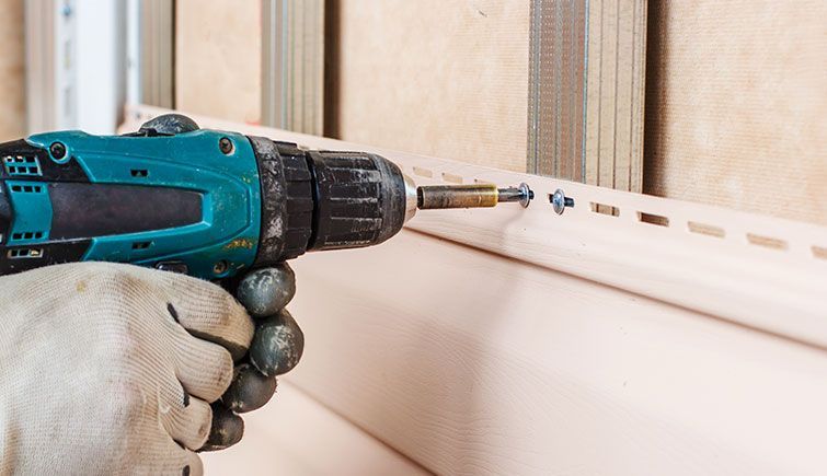 A person is using a drill to install siding on a wall.