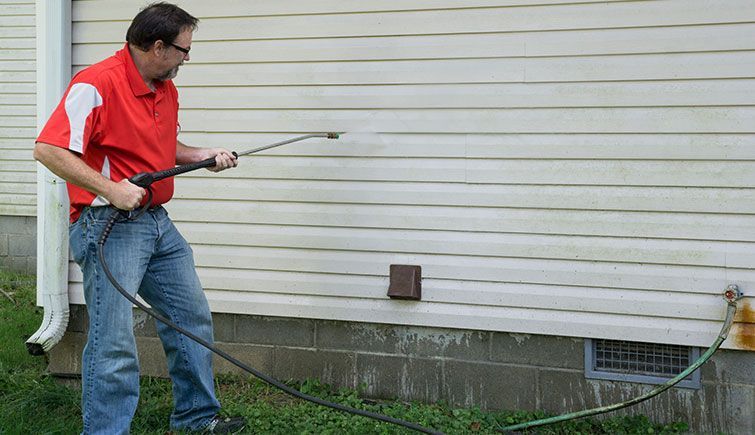 A man is cleaning the side of a house with a pressure washer.