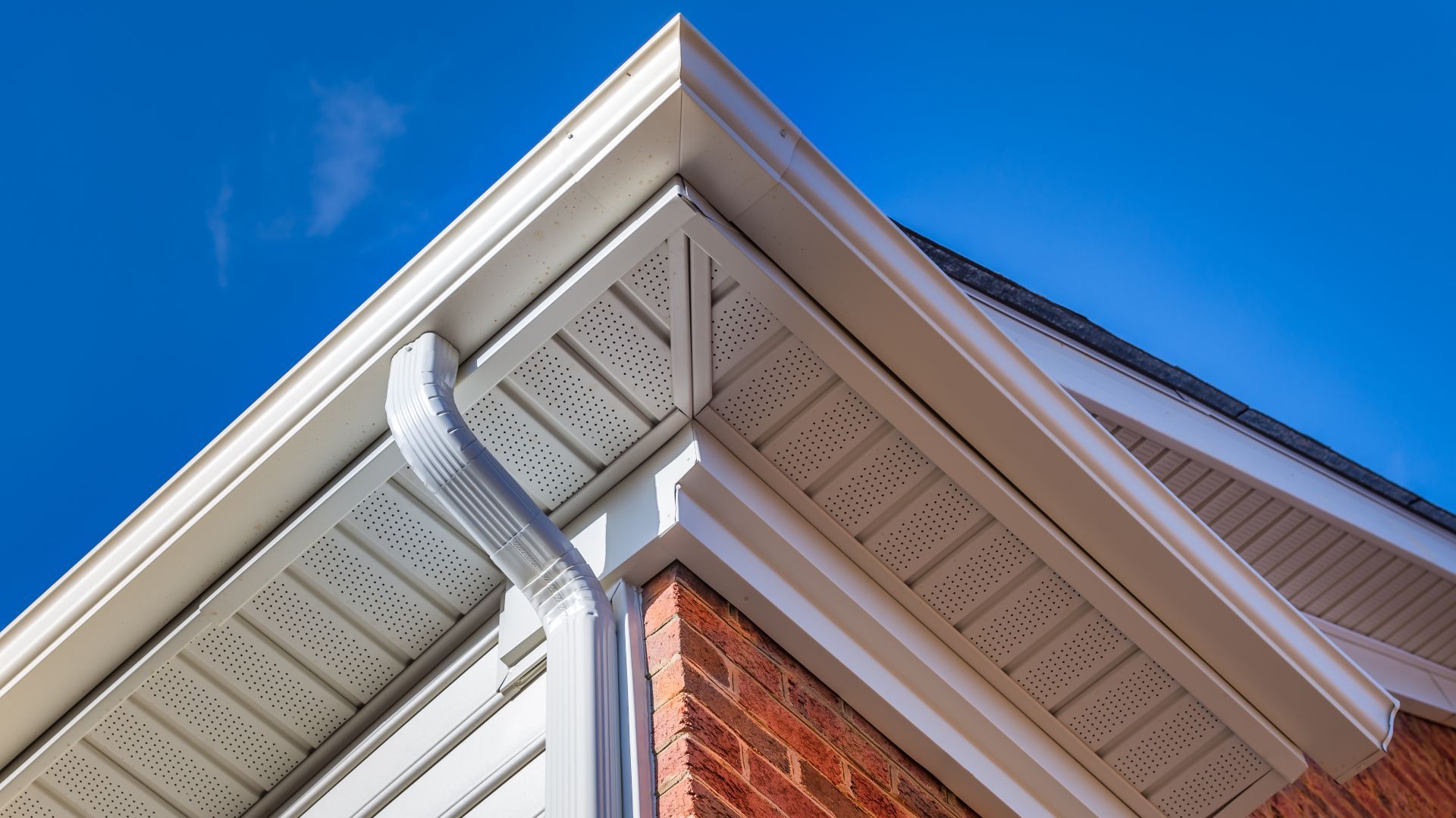 A brick building with a white gutter and a blue sky in the background