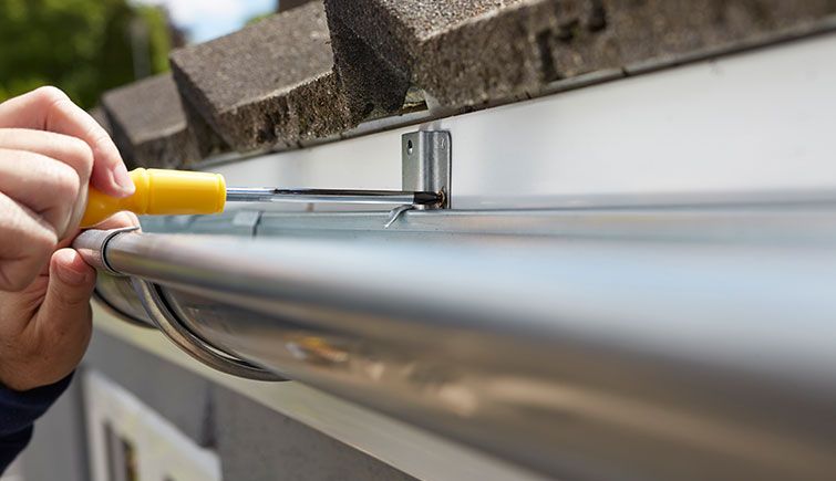 A person is fixing a gutter with a screwdriver.