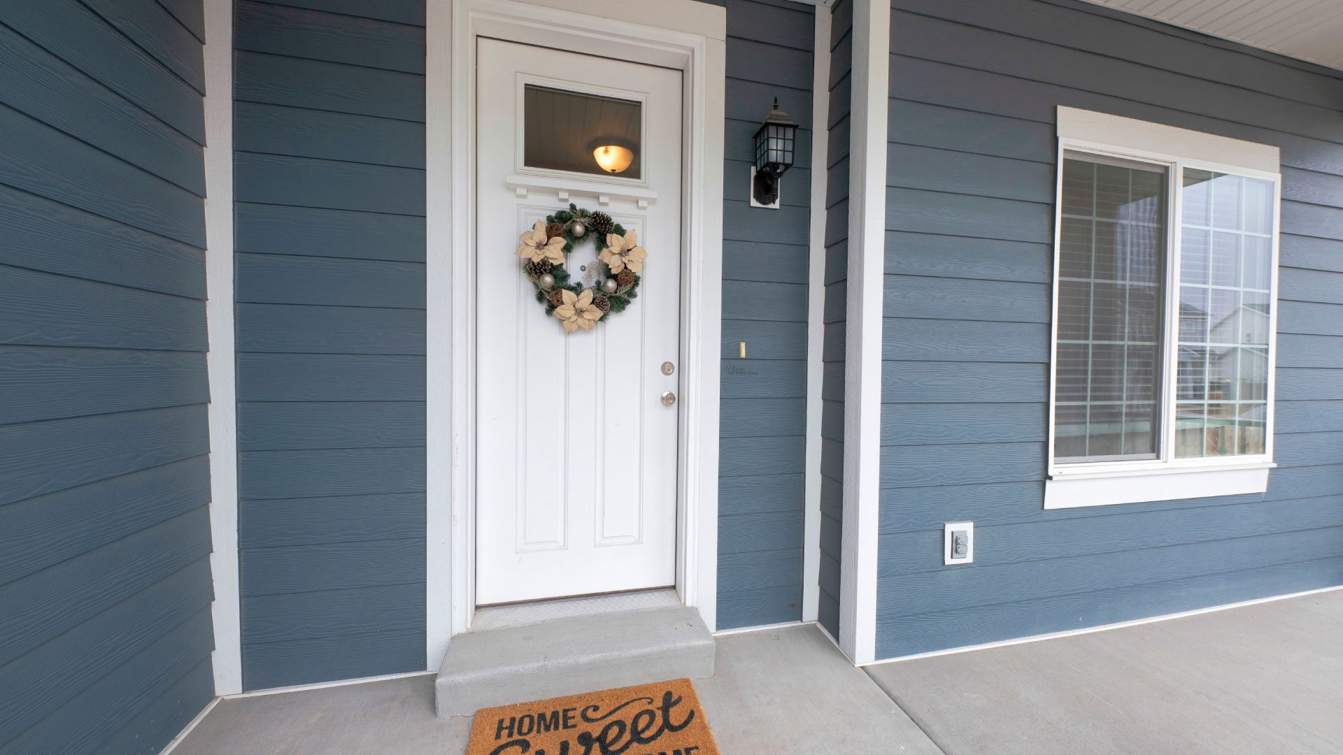 A blue house with a white door and a welcome mat on the porch.