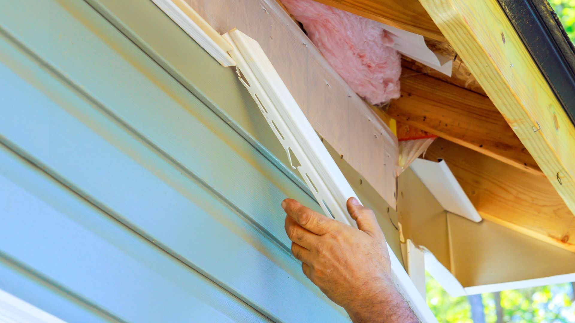 A man is installing siding on the side of a house.