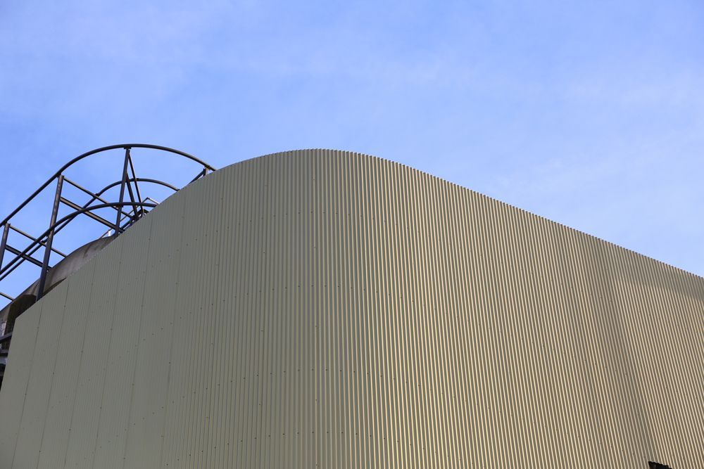 Façade d'un bâtiment en tôle ondulée incurvée se détachant sur un ciel bleu, avec une structure métallique sombre visible.