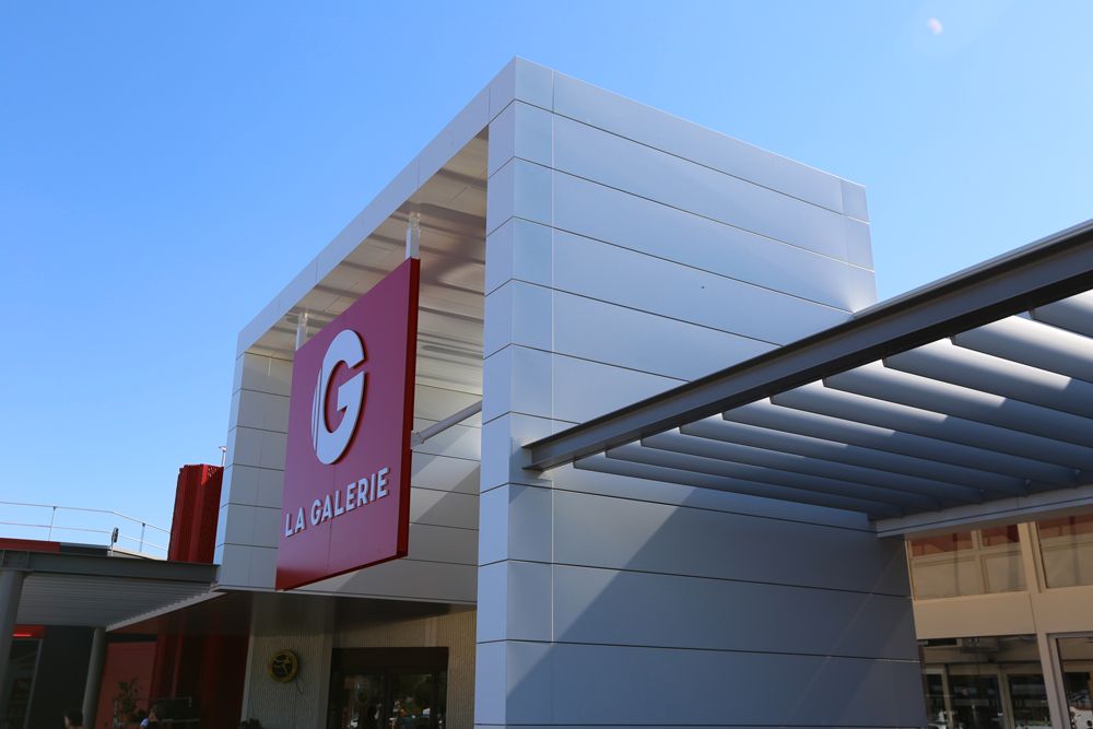 Enseigne « La Galerie » sur un immeuble moderne aux accents rouges et blancs, sur fond de ciel bleu.