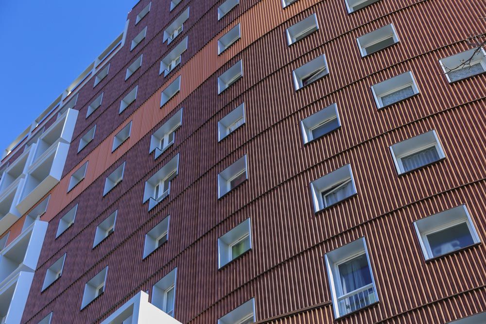 Grand immeuble brun aux nombreuses fenêtres carrées se détachant sur un ciel bleu clair.
