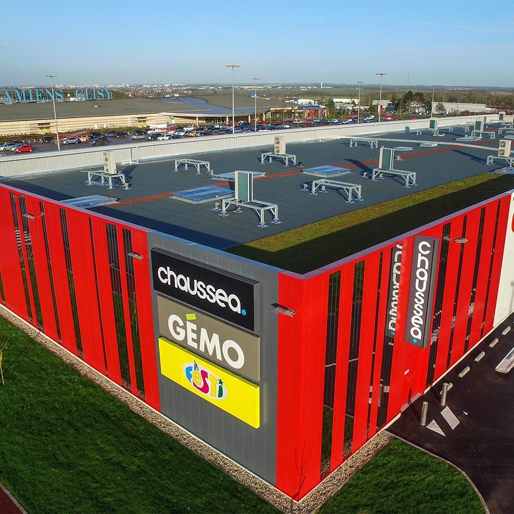 Centre commercial rouge et gris avec de grandes enseignes de marques : Chaussea, Gémo et Eurodif, et parking.