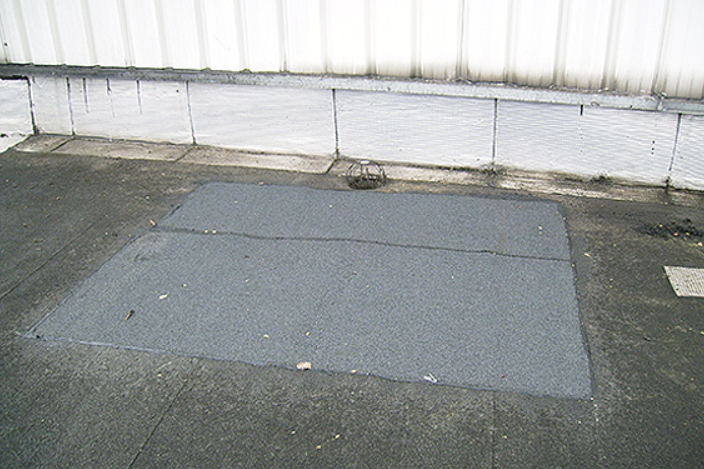 Une plaque d'asphalte sur une surface en béton contre un mur blanc.