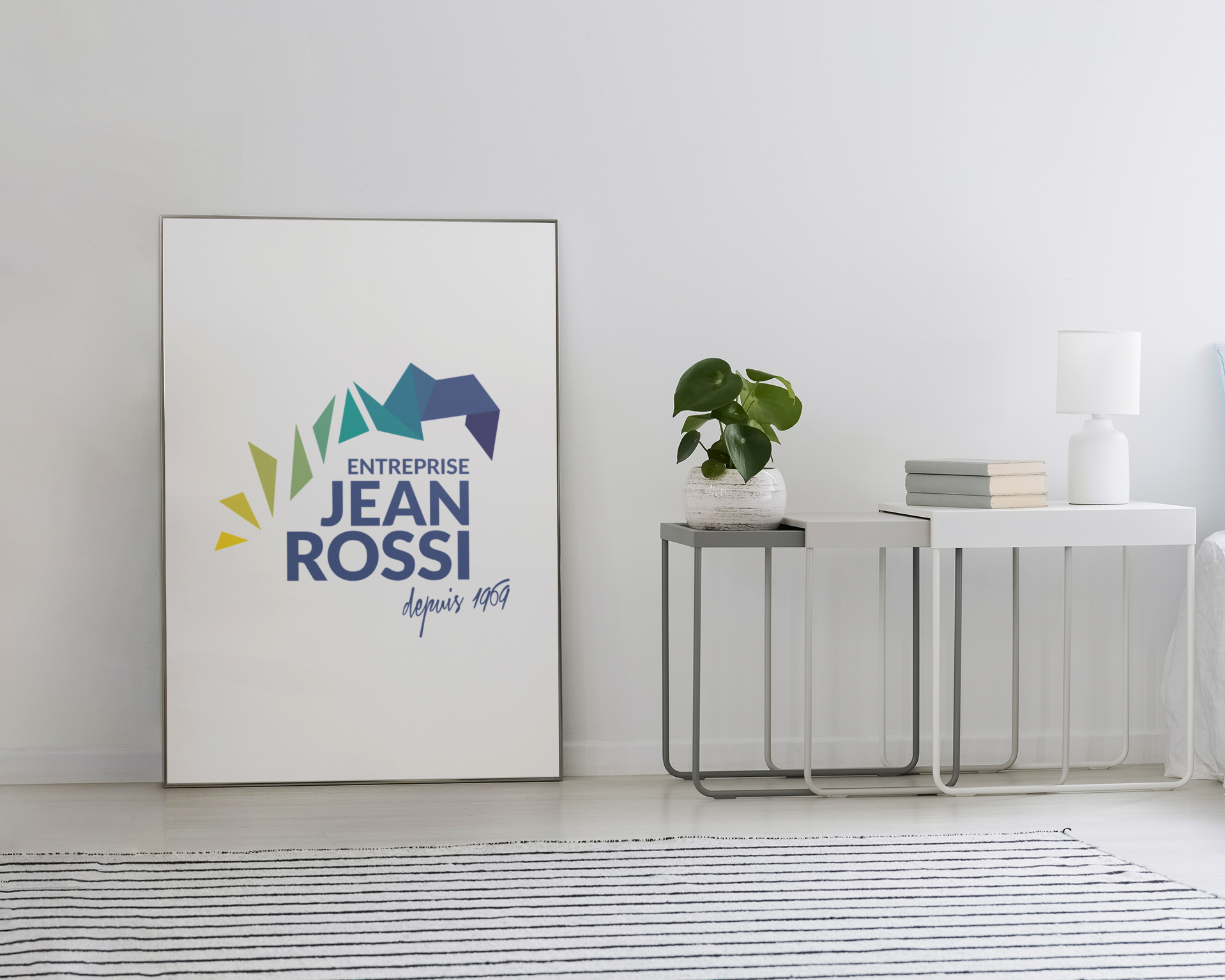 Une affiche portant le logo « Entreprise Jean Rossi » est appuyée contre un mur blanc, à côté d'une table avec une plante.