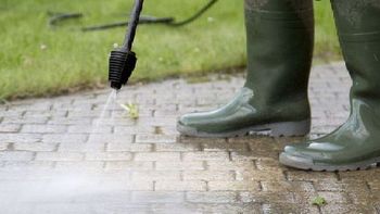 A person is using a high pressure washer to clean a brick walkway.