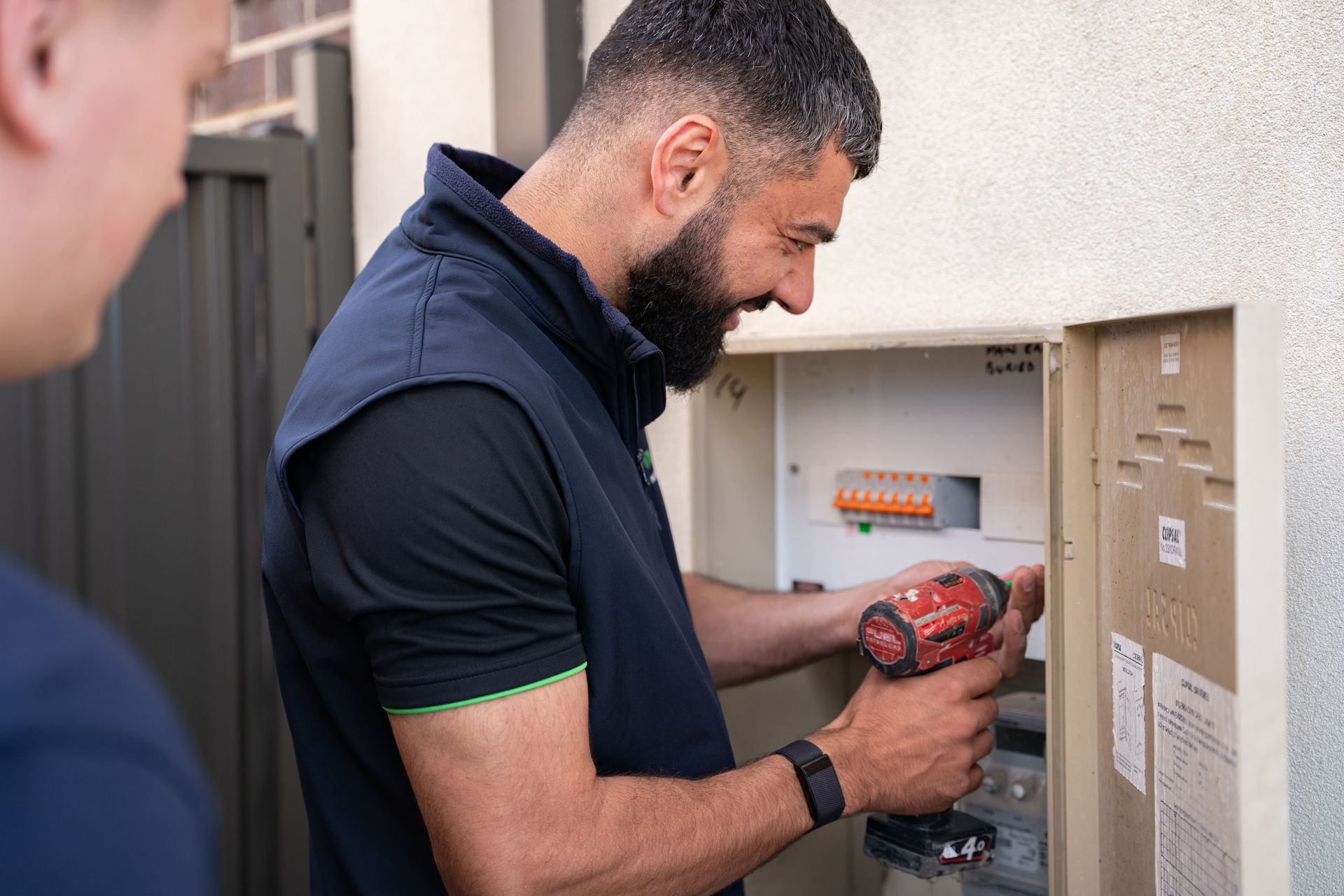 A man is working on an electrical box with a drill.