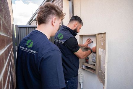 Two men are working on an electrical box on the side of a building.
