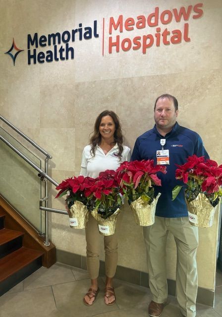 A man and a woman holding poinsettia flowers in front of memorial meadows hospital
