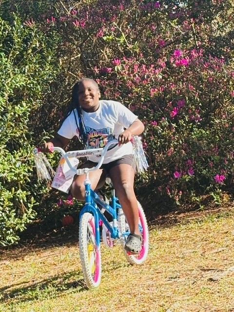 A young girl is riding a blue bike with pink wheels