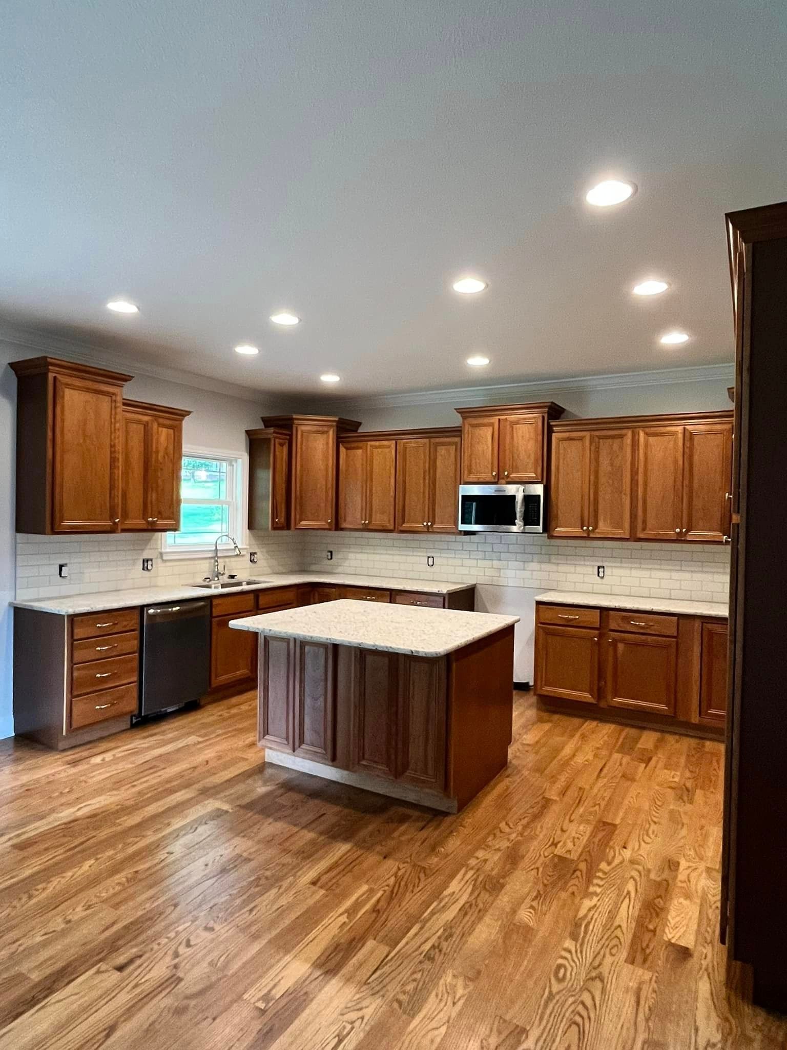 A kitchen with wooden cabinets and hardwood floors and a large island in the middle.