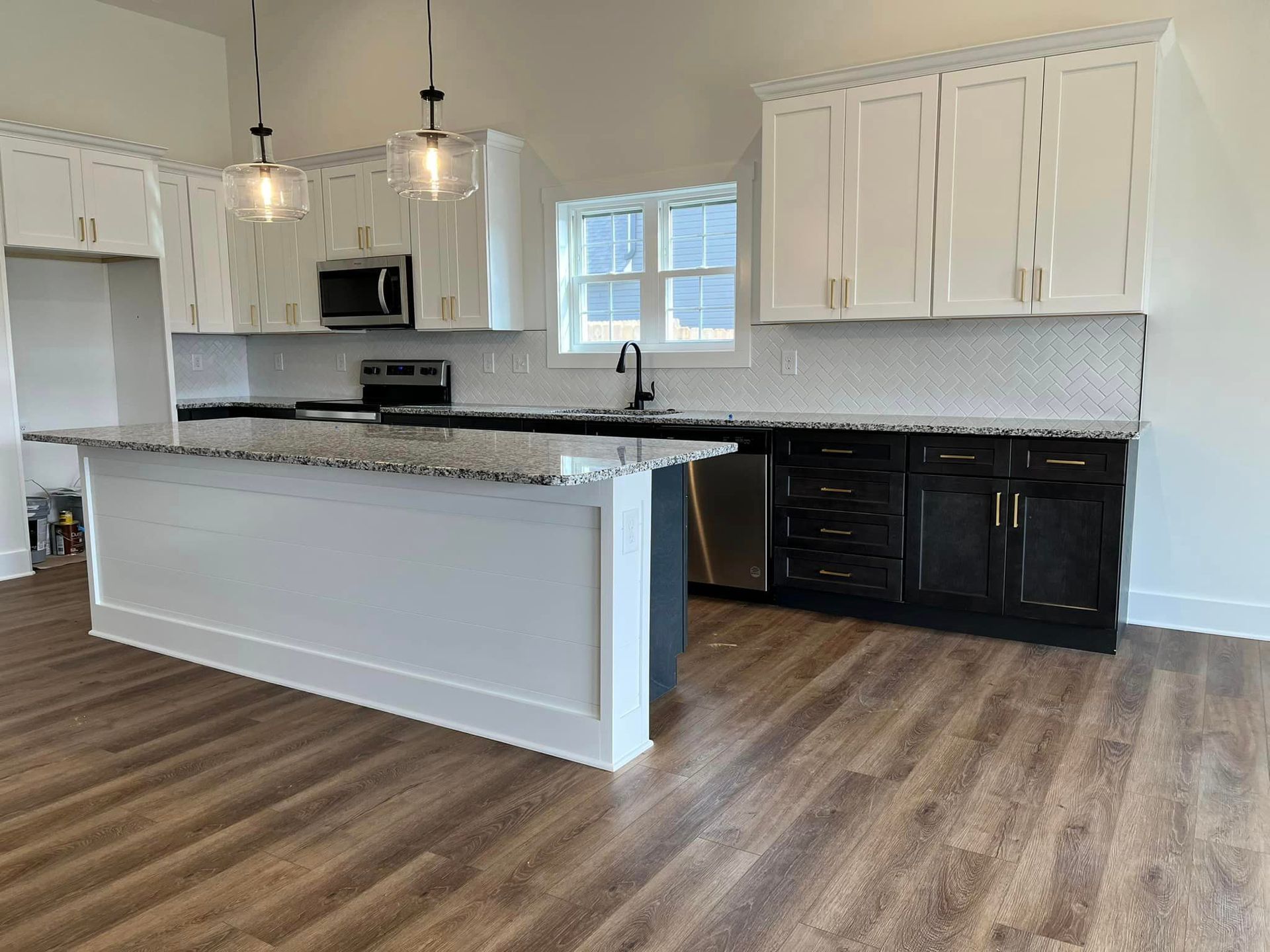 A kitchen with white cabinets , black cabinets , granite counter tops and stainless steel appliances.