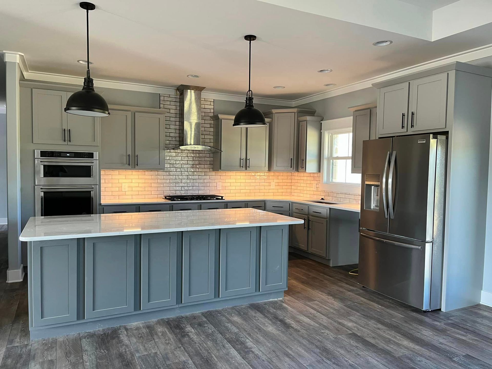 A kitchen with gray cabinets , stainless steel appliances , and a large island.