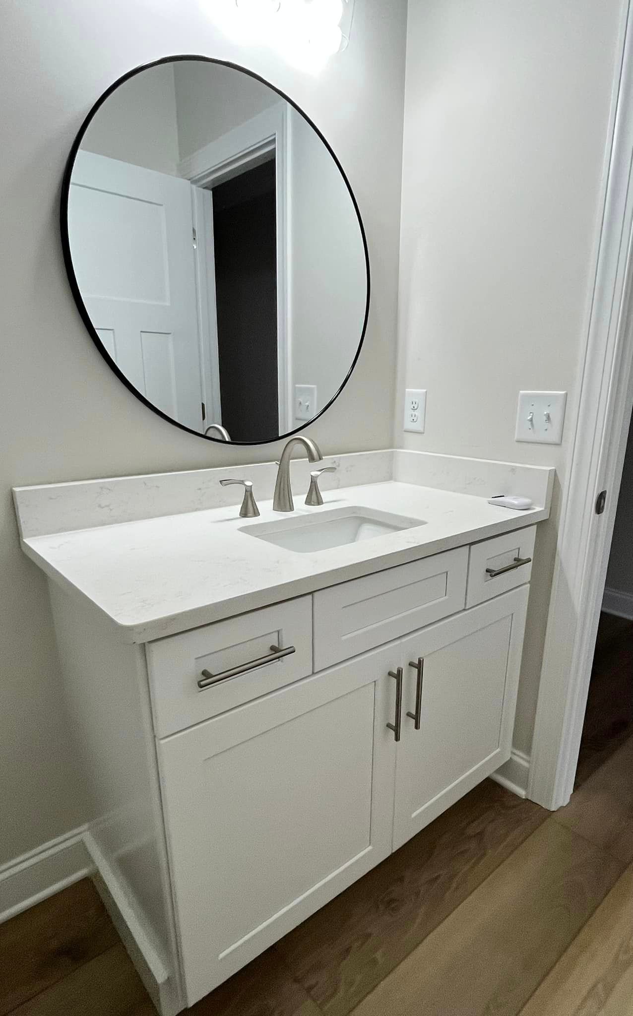 A bathroom sink with a round mirror above it.