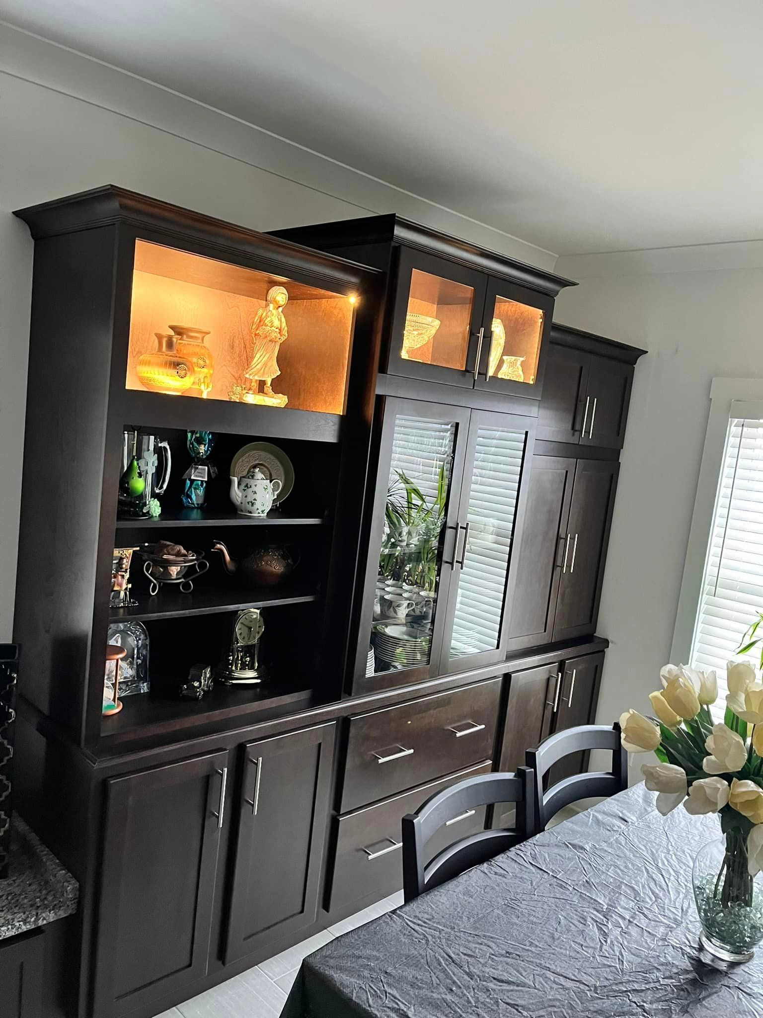 A dining room with a table , chairs , a hutch and a window.