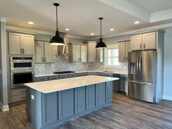 A kitchen with gray cabinets , stainless steel appliances , and a large island.