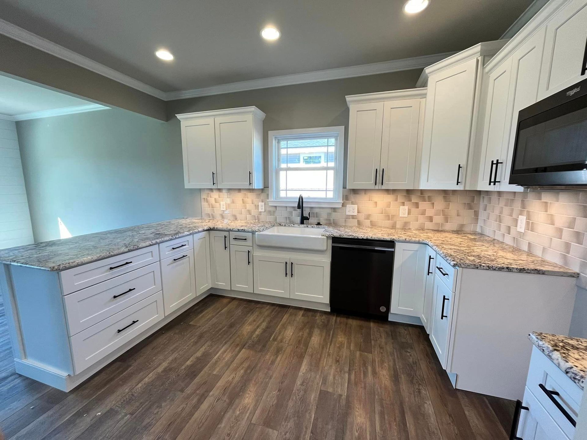 A kitchen with white cabinets , granite counter tops , a sink and a microwave.