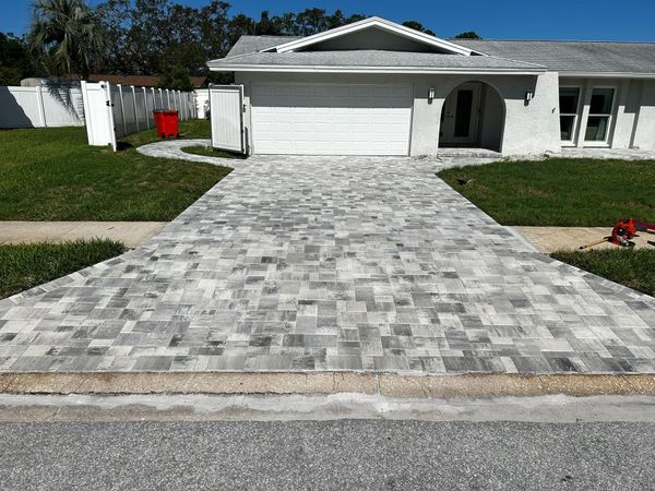A white house with a large, newly installed grey paver driveway extending from the street to the garage.
