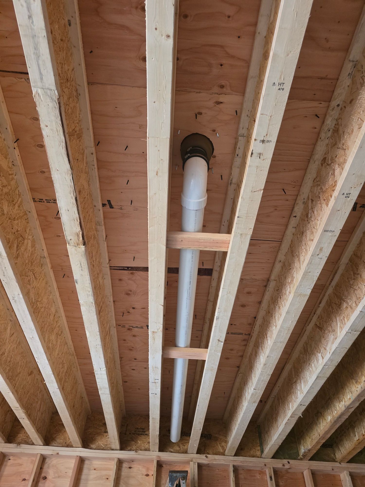 White PVC pipe suspended between wooden ceiling joists, extending up to a black vent fitting.